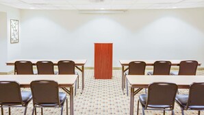 A conference room with a long table, chairs, a podium, and a patterned floor. - Microtel Inn & Suites by Wyndham Saraland/North Mobile (Saraland)