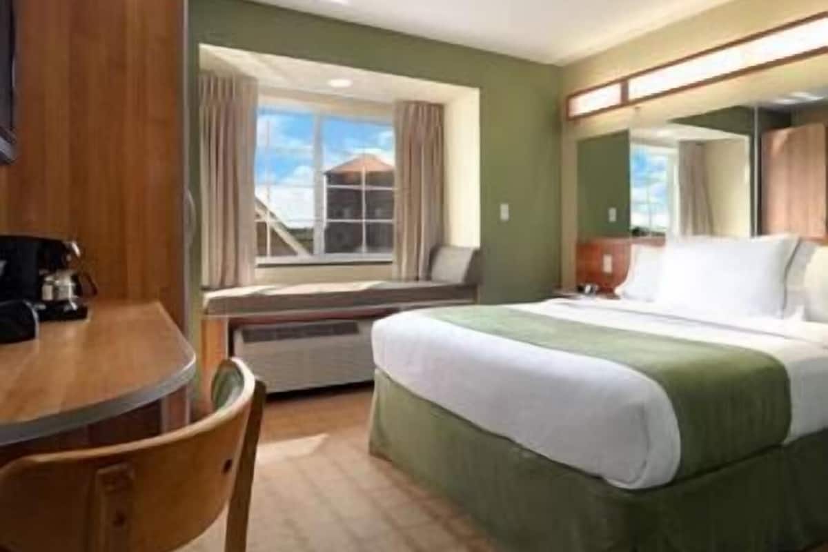 Une chambre d’hôtel comprenant un lit, un bureau, une chaise, une fenêtre avec des rideaux et une vue sur un bâtiment à l’extérieur.