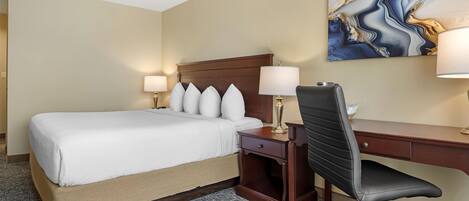A hotel room with a bed, a desk, a chair, and a painting on the wall.