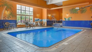 Una piscina interior con paredes de azulejos, un mural de un pájaro en una rama, y una zona de estar con sillas y mesas.
