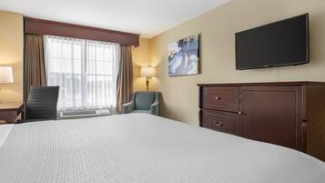 Een hotelkamer met een groot bed, een bureau met een lamp, een stoel, een aan de muur bevestigde televisie en een schilderij.