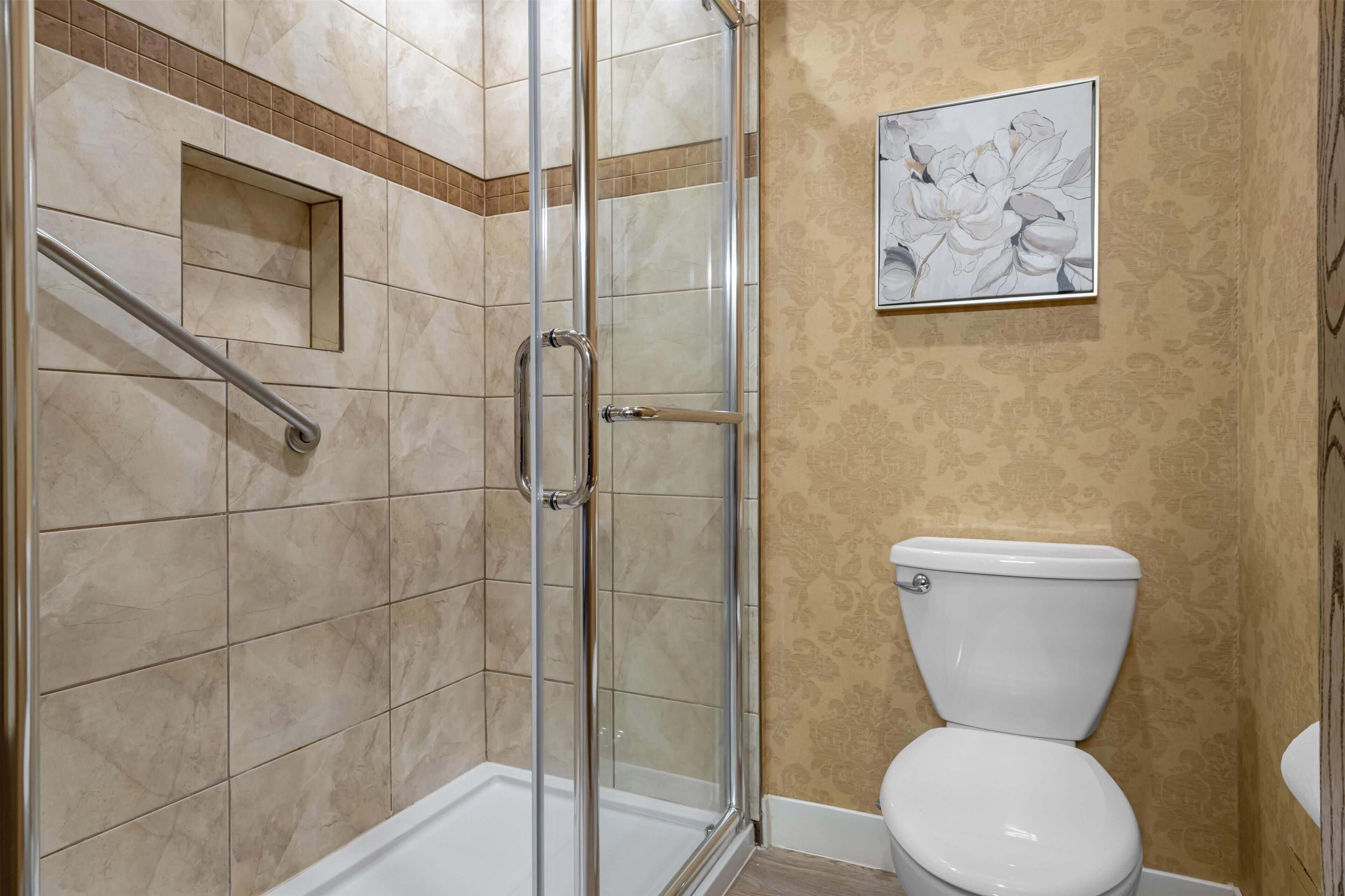 A bathroom with a glass-enclosed shower, a toilet, and a framed floral artwork on the wall.