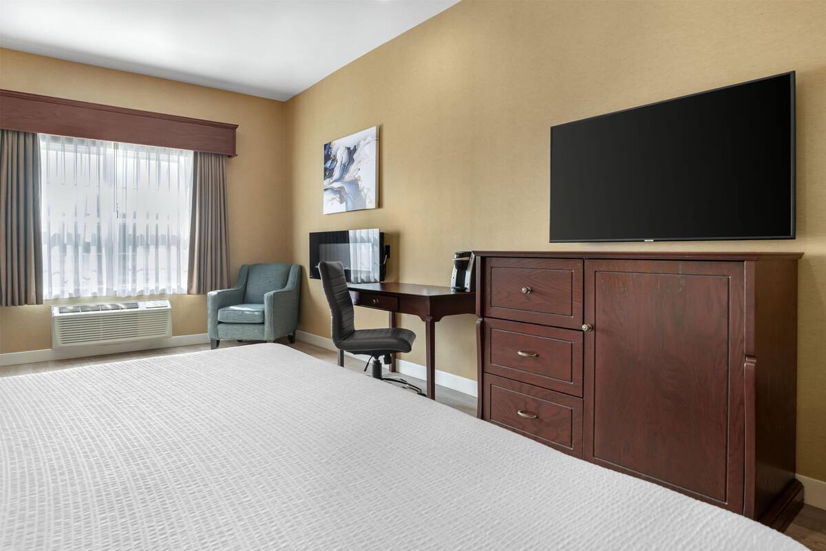 Une chambre d’hôtel avec un grand lit, un bureau, une chaise, une télévision et une armoire.