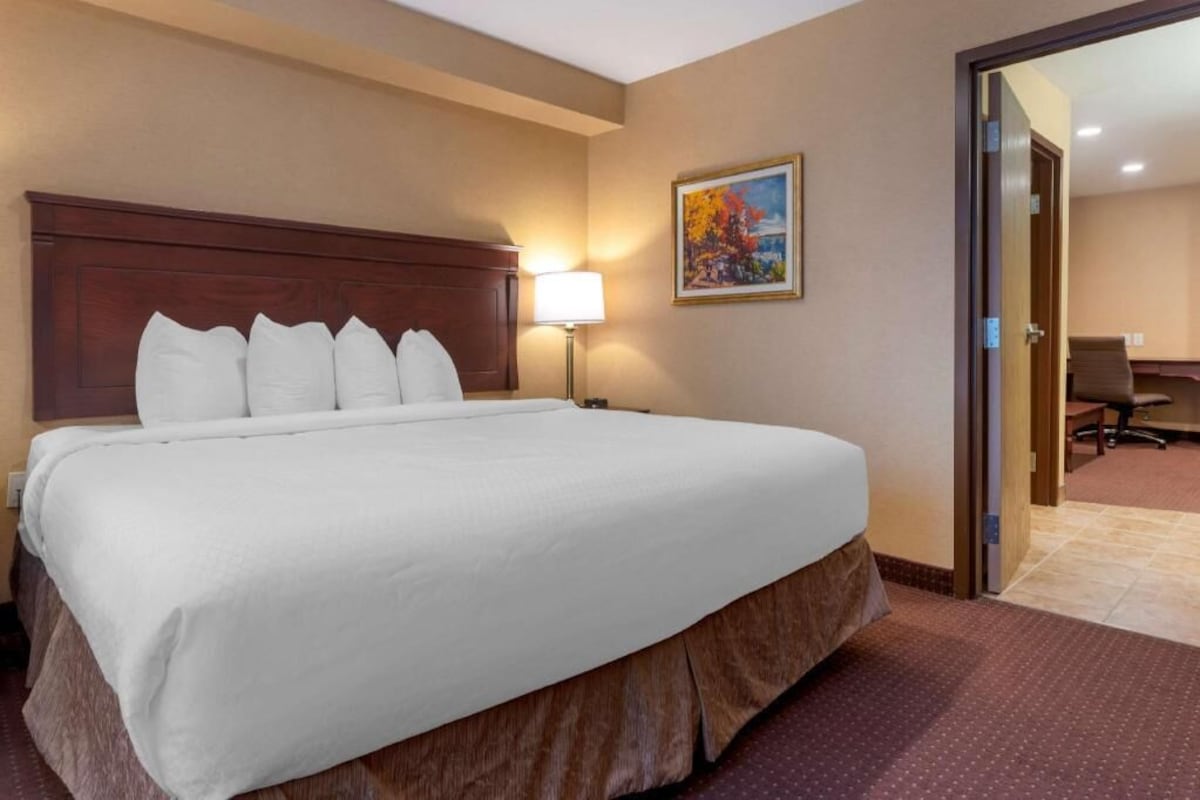 Ein Hotelzimmer mit einem großen Bett, einem Nachttisch mit Lampe, einem Gemälde an der Wand und einer Tür zu einem Konferenzraum.