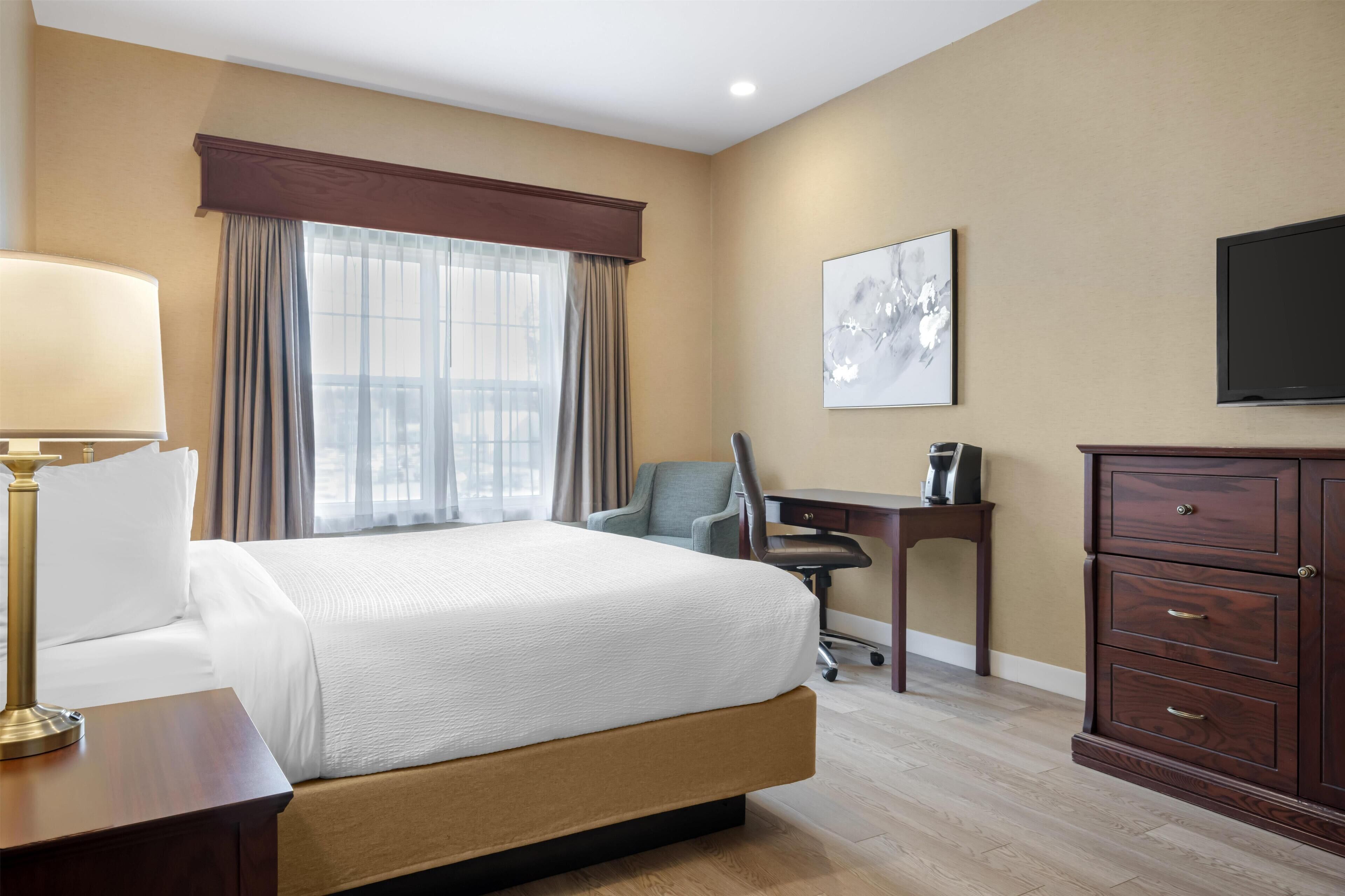 A hotel room with a large bed, a desk, a chair, a TV, and a cabinet.