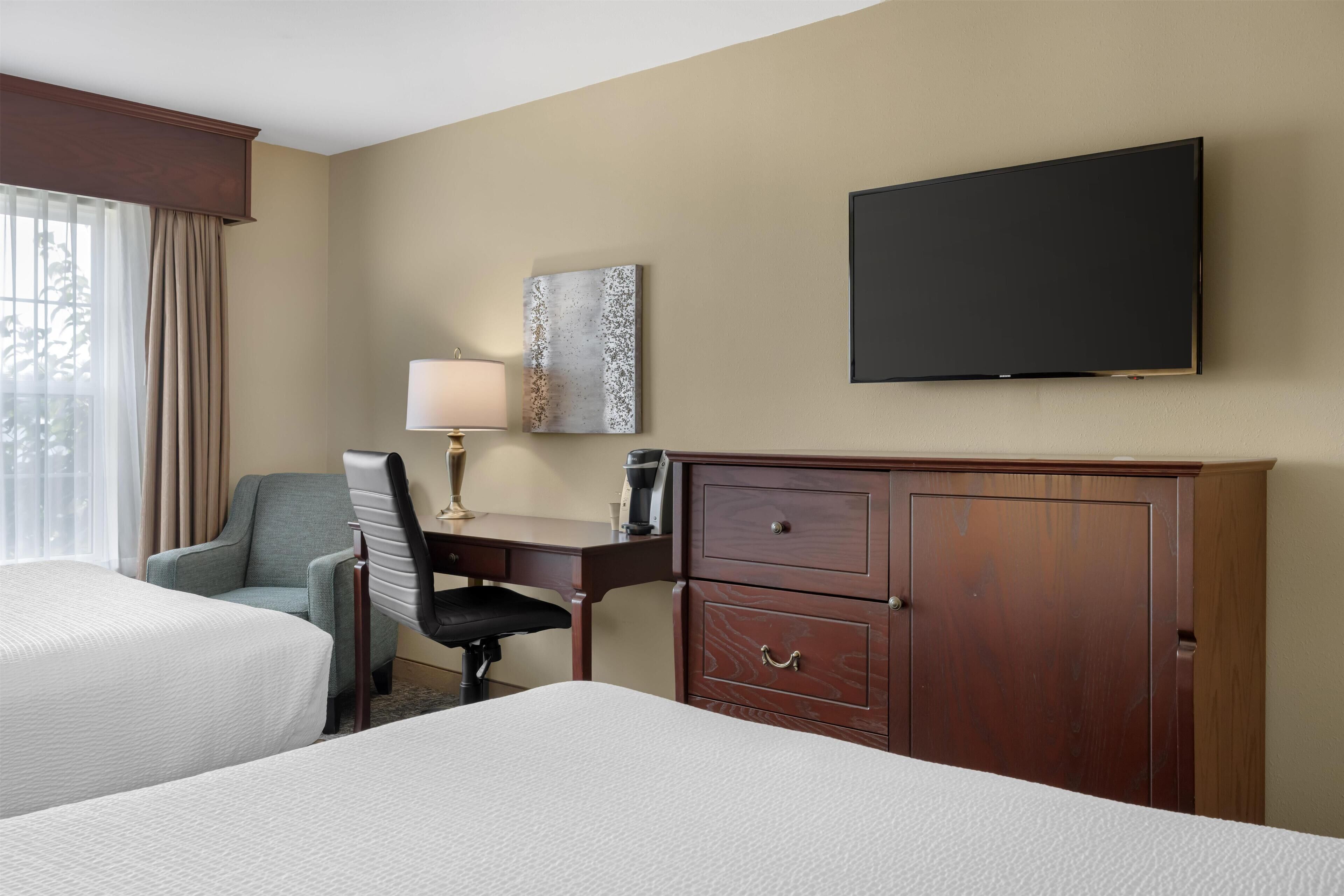 A hotel room with two beds, a desk, a chair, a TV, and a cabinet.