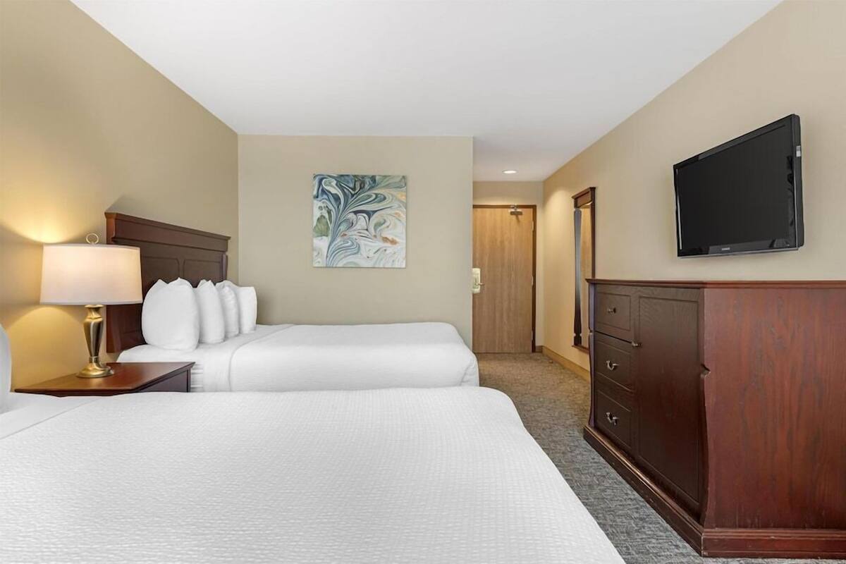 Une chambre d’hôtel avec un lit, un bureau avec une lampe, une télévision, une armoire et un tableau au mur.