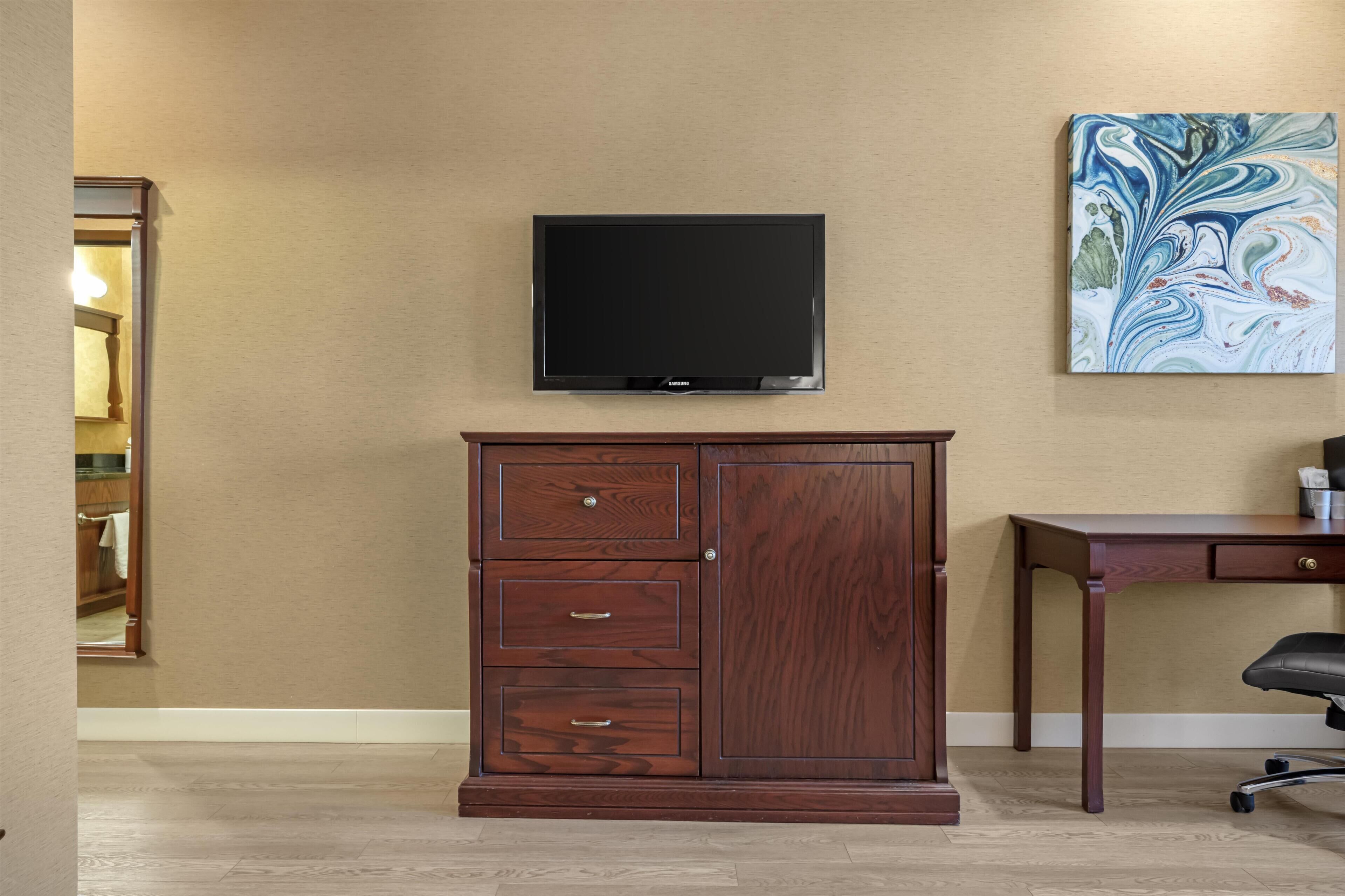 Une pièce comprenant un meuble en bois, un téléviseur fixé au mur et un bureau avec une chaise.