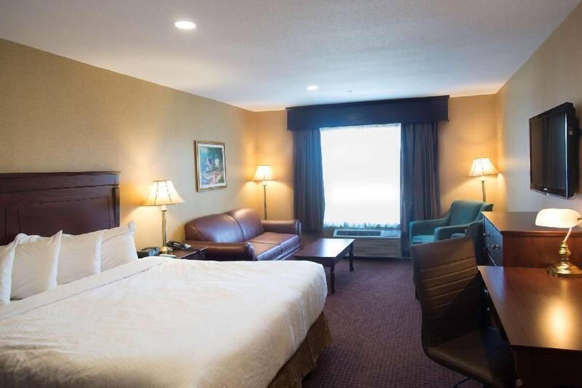 Une chambre d’hôtel comprenant un lit, un canapé, un bureau, une chaise, une télévision et une fenêtre avec des rideaux.
