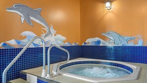 Jacuzzi con un mural de delfines en la pared, azulejos azules y una escalera de metal.