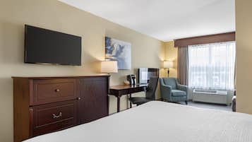 A hotel room with a large bed, a desk with a chair, a TV mounted on the wall, a painting, and a window with curtains.