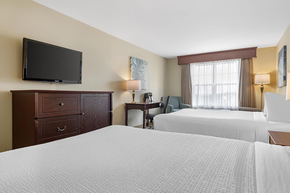 Une chambre d’hôtel avec deux lits, un téléviseur fixé au mur, un bureau avec une chaise et une fenêtre avec des rideaux.