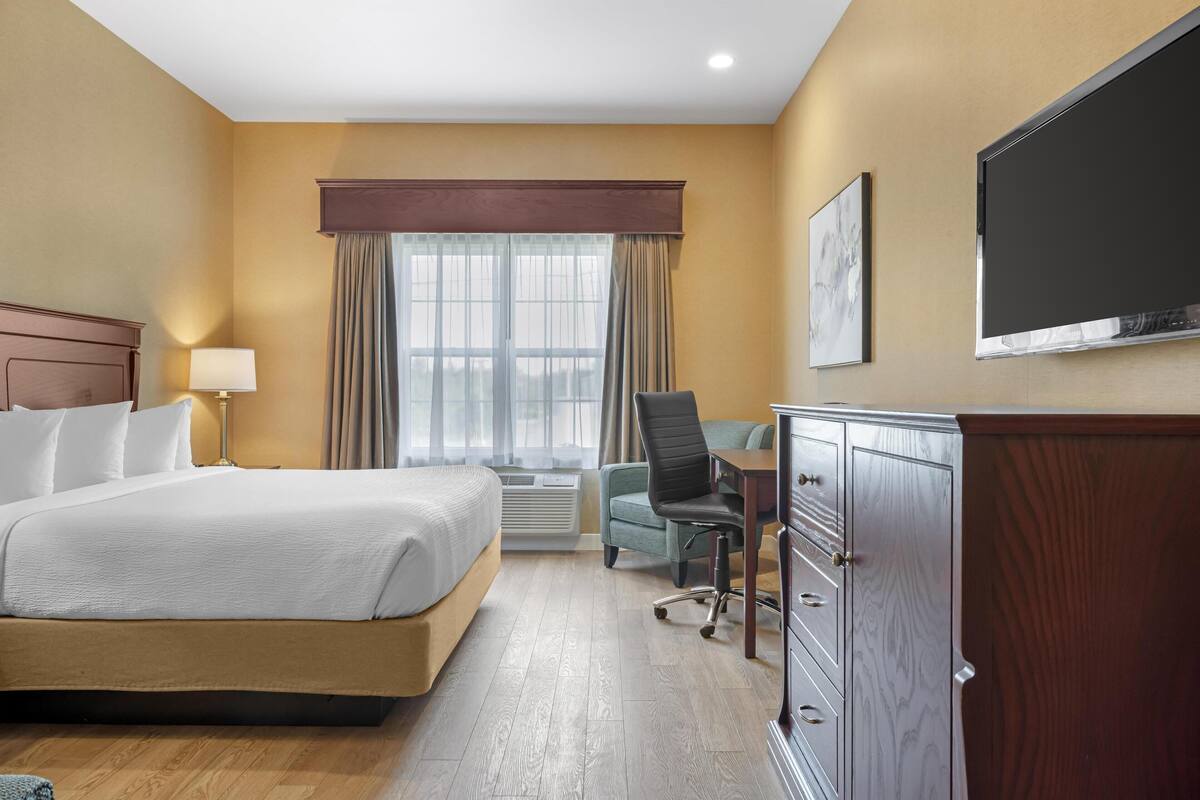 Une chambre d’hôtel équipée d’un lit, d’un bureau, d’une chaise, d’une armoire et d’un téléviseur fixé au mur.