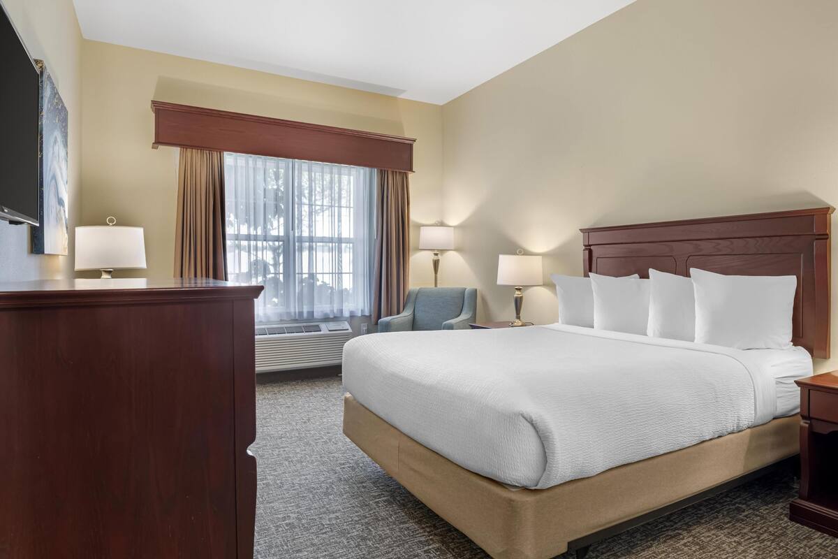 Une chambre d’hôtel avec un grand lit, deux lampes de chevet, un bureau avec une lampe, une chaise et une grande fenêtre avec des rideaux.