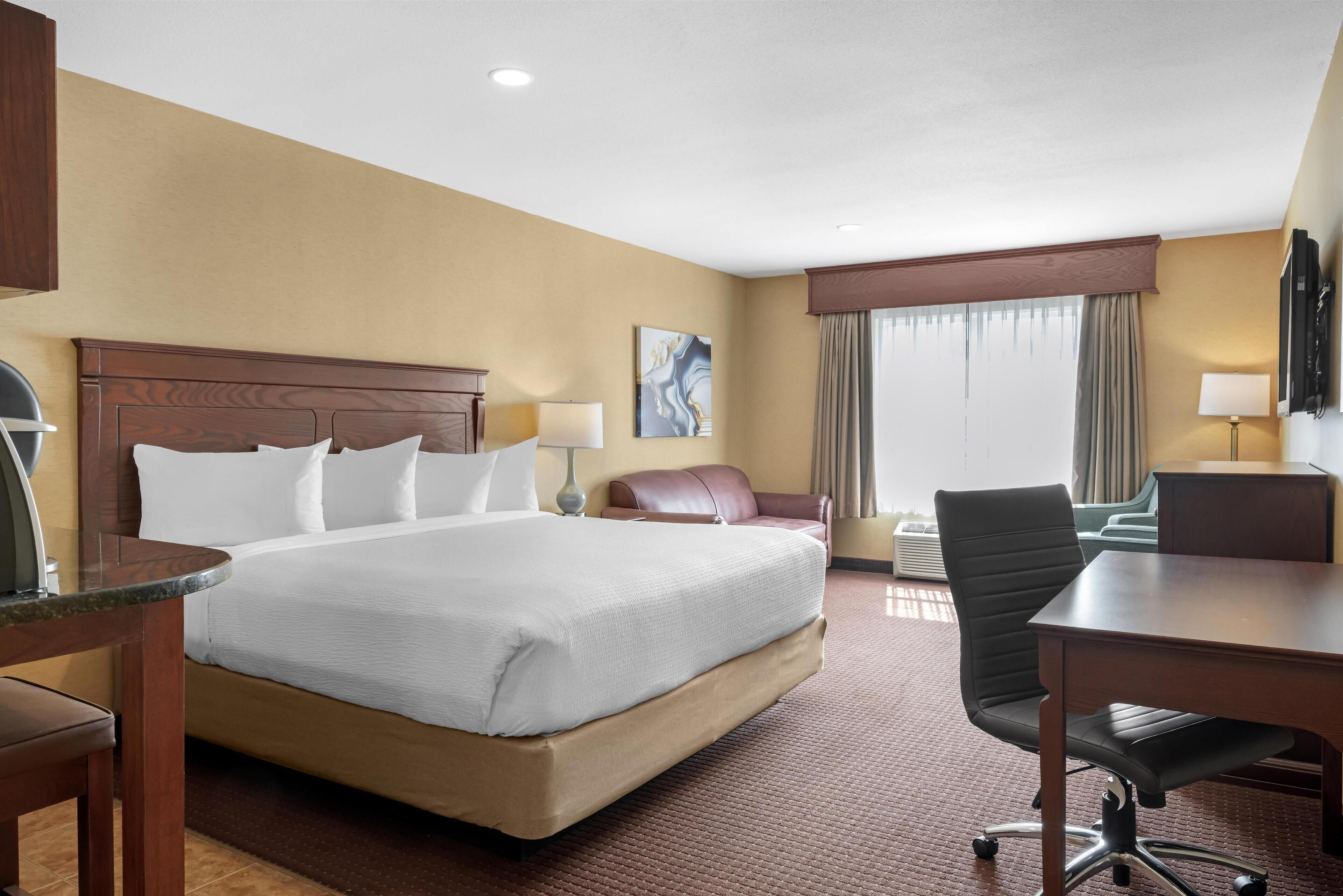 A hotel room with a large bed, a desk, a chair, a TV, and a window with curtains.