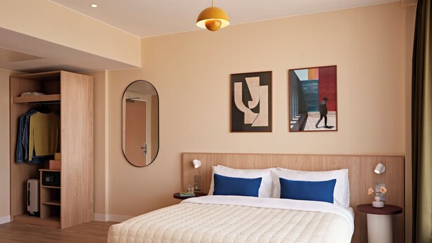 Una habitación de hotel con cama, mesitas de noche, armario, espejo y cuadros en las paredes.
