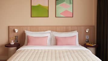 A hotel room with a bed, two bedside tables, a nightstand, a wall-mounted light, and two framed artworks.