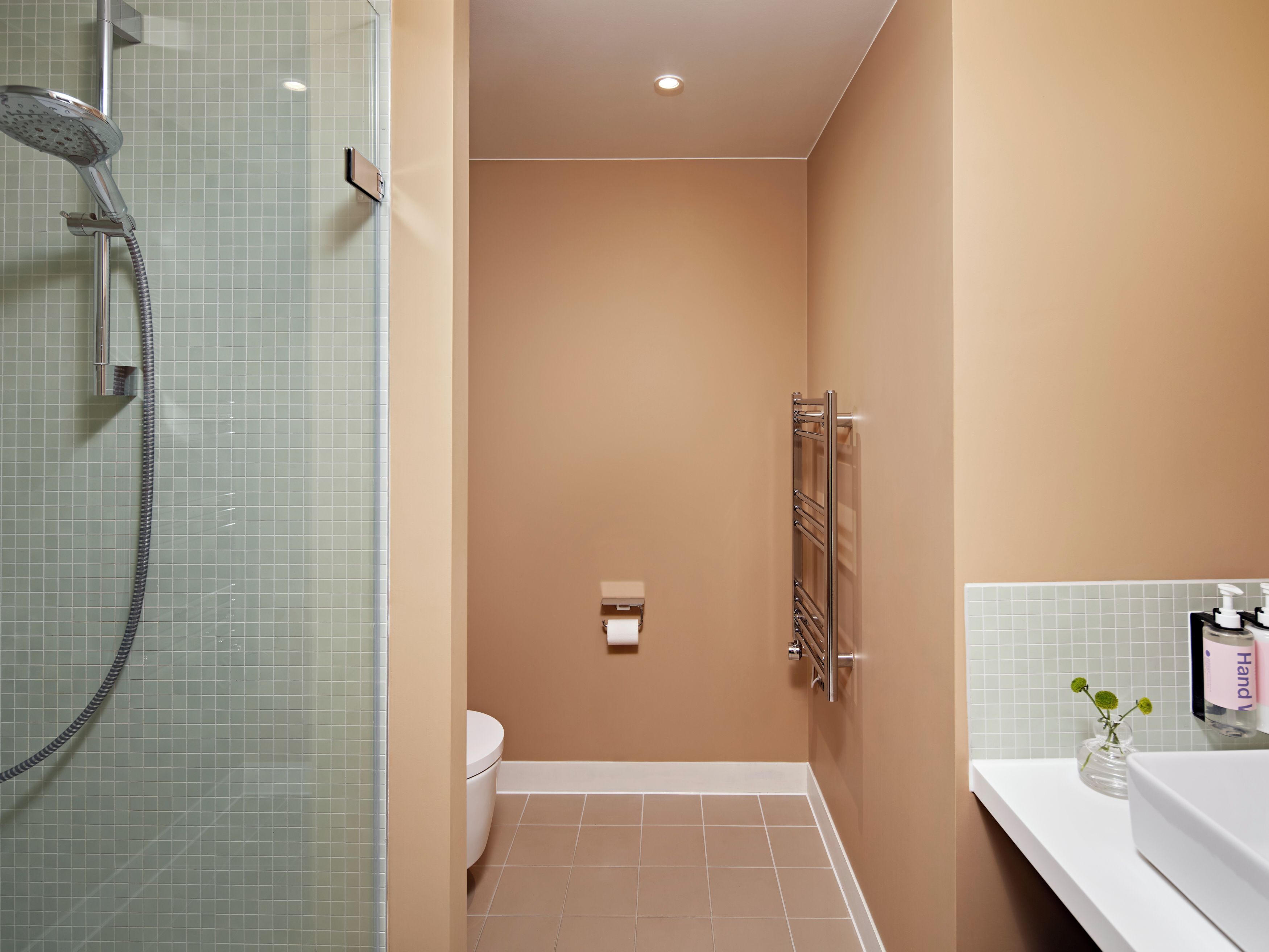 A bathroom with a glass shower enclosure, a toilet, a towel rack, and a sink with a vase of flowers.