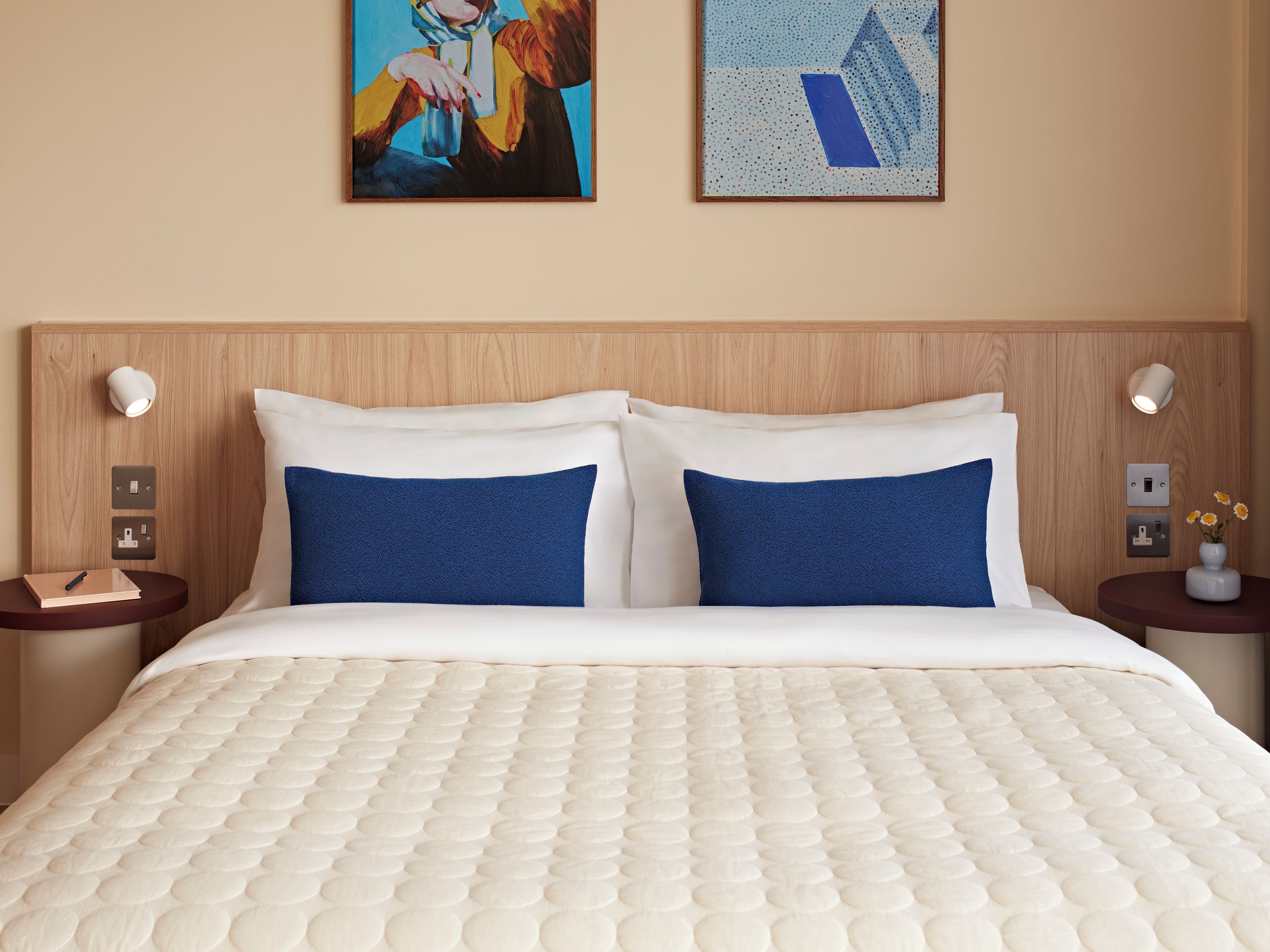 Une chambre d’hôtel avec un lit, deux oreillers, une table de chevet, une lampe et un tableau au mur.