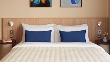 Una camera d'albergo con un letto, due cuscini, un comodino, una lampada e un quadro appeso al muro.