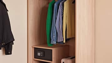 A wooden wardrobe with hanging clothes, a small shelf with books, and a suitcase.