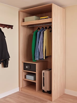 Un armario de madera con ropa colgada, un pequeño estante con libros y una maleta.