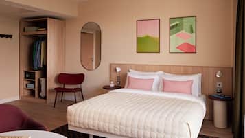 A hotel room with a bed, a chair, a desk, a wardrobe, and two paintings on the wall.
