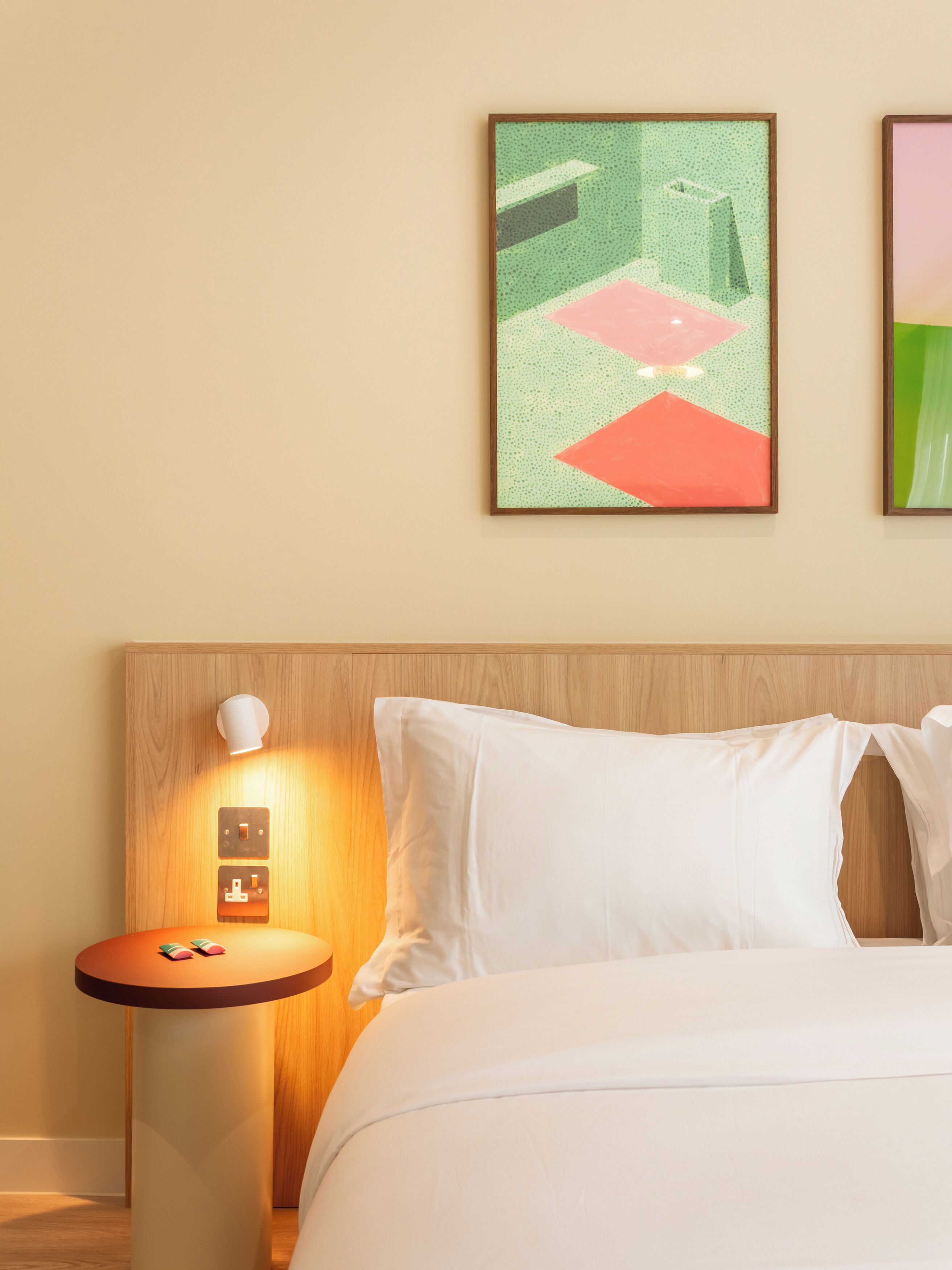 A hotel room with a bed, a nightstand, and two framed artworks on the wall.