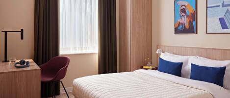 Hotellihuone, jossa on sänky, työpöytä, tuoli, vaatekaappi ja ikkuna, jossa on verhot.