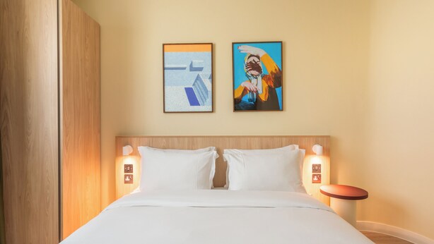A hotel room with a large bed, two wall-mounted light fixtures, and two framed artworks above the bed. - Numa Brighton Pavilion (Brighton)