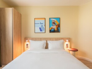 Una habitación de hotel con una cama grande, dos lámparas de pared y dos cuadros enmarcados sobre la cama.