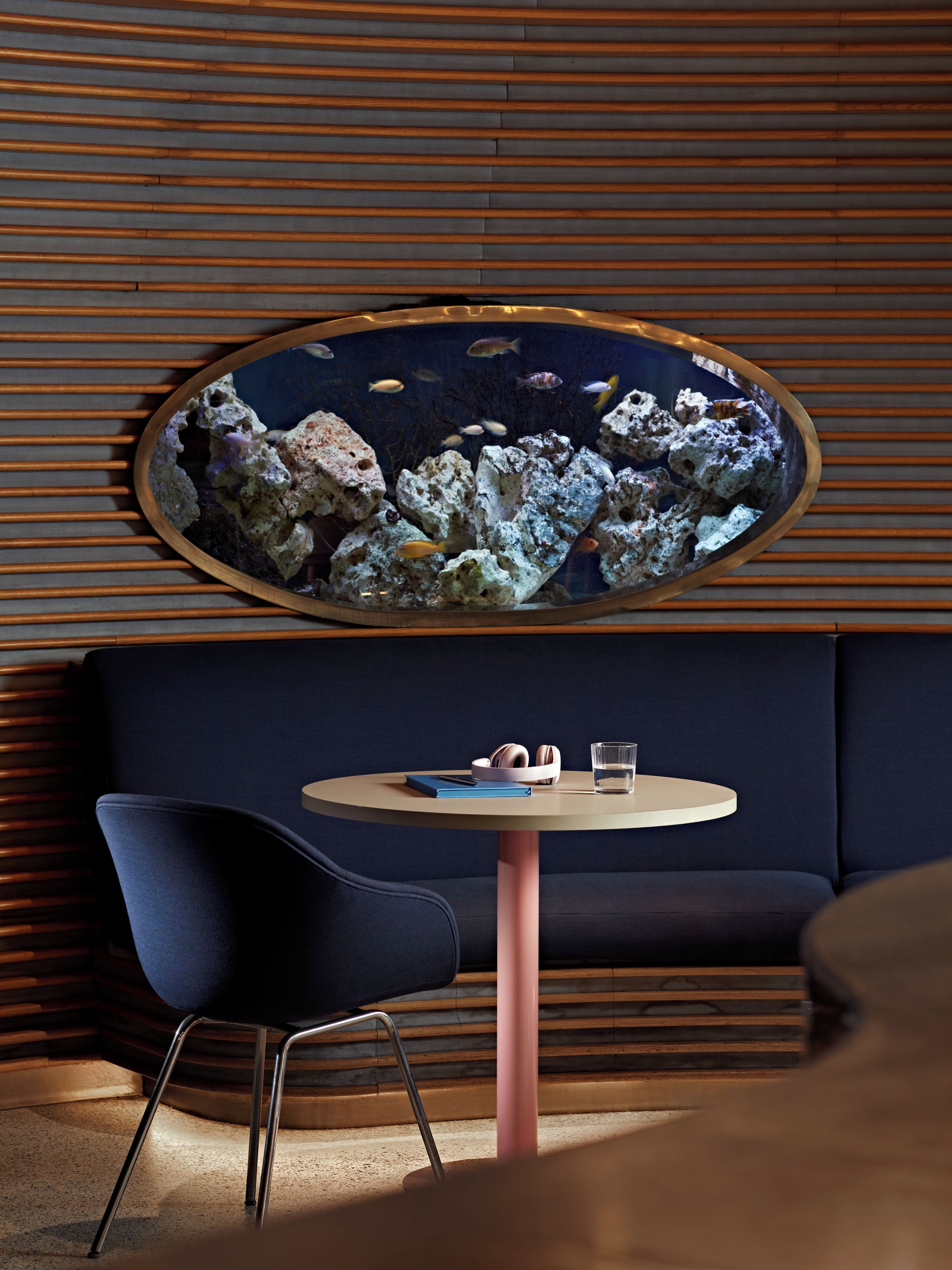 Un intérieur moderne avec une table ronde, une chaise bleue, un canapé et un aquarium fixé au mur.