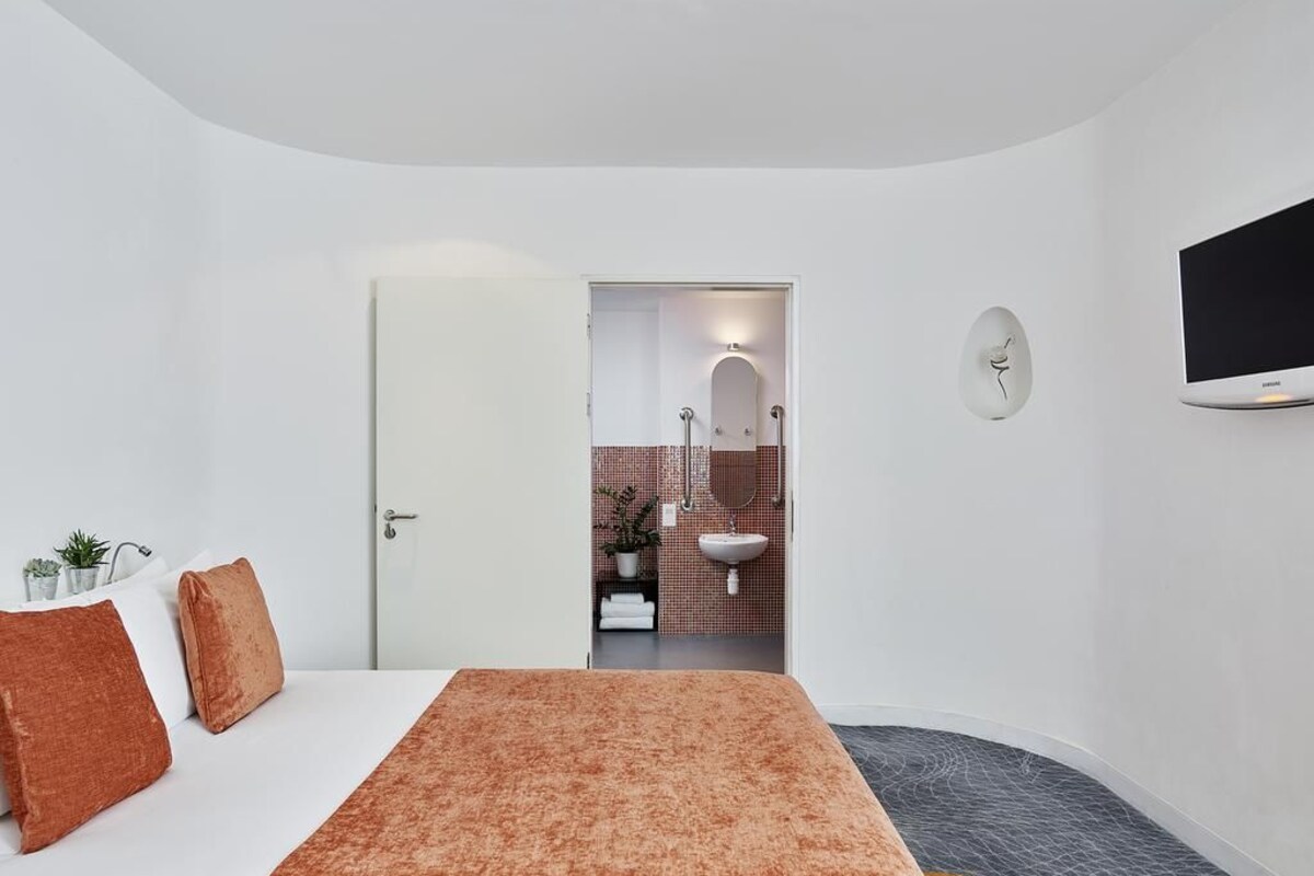 Un dormitorio con cama, televisión y baño visible a través de una puerta abierta.