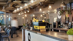 Interior de una cafetería con mostrador, zona de estar y lámparas colgantes.