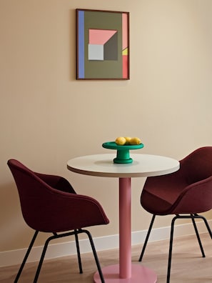 Una habitación con una mesa redonda, dos sillas, una obra de arte en la pared y un frutero sobre la mesa.