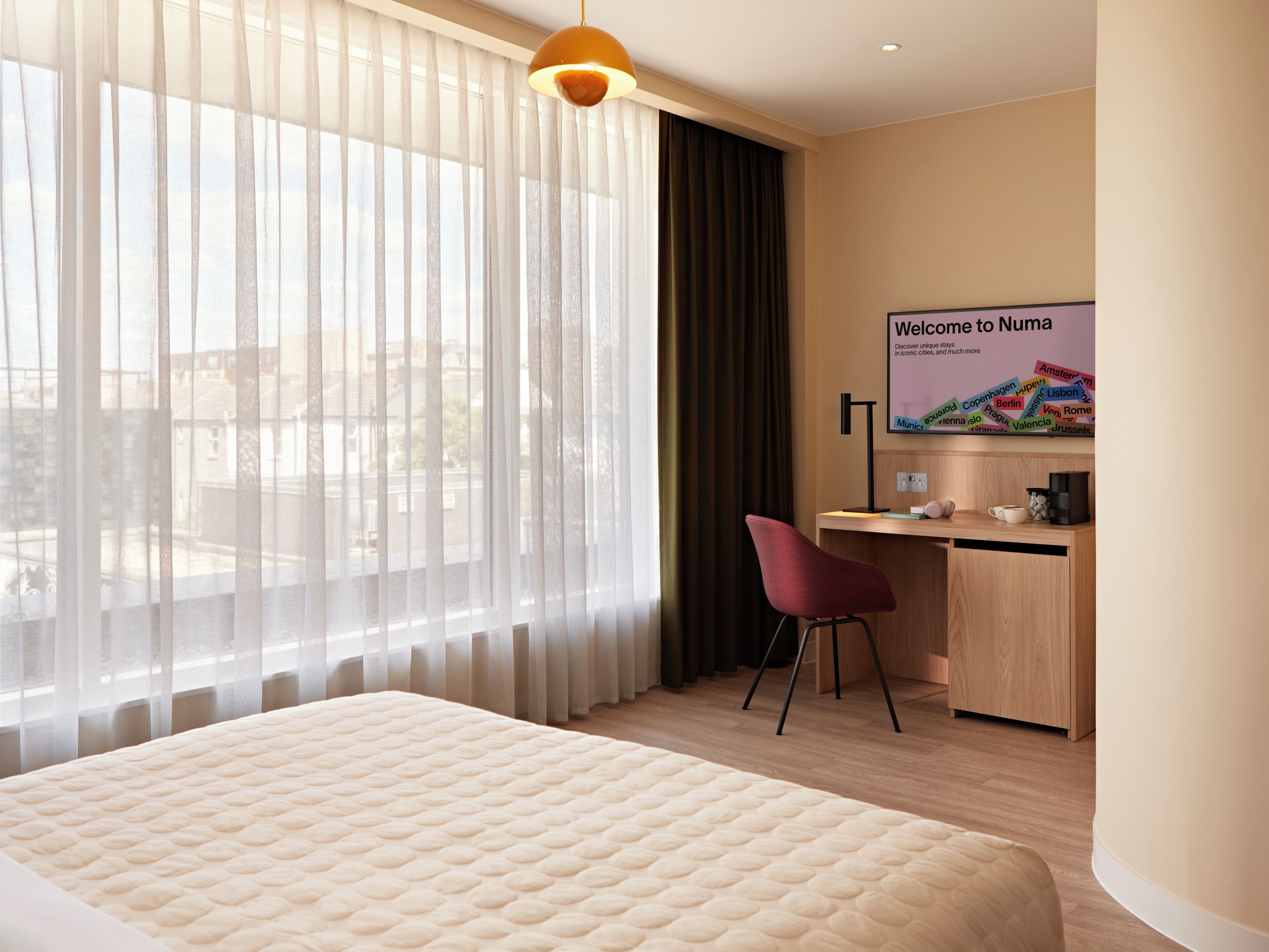 A hotel room with a bed, a desk, a chair, a television, and a window with curtains.