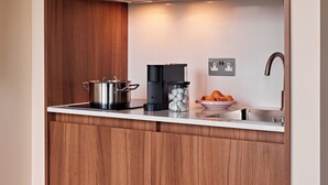 Una cocina compacta con armarios de madera, una olla de acero inoxidable, una cafetera y un cuenco con fruta en la encimera.