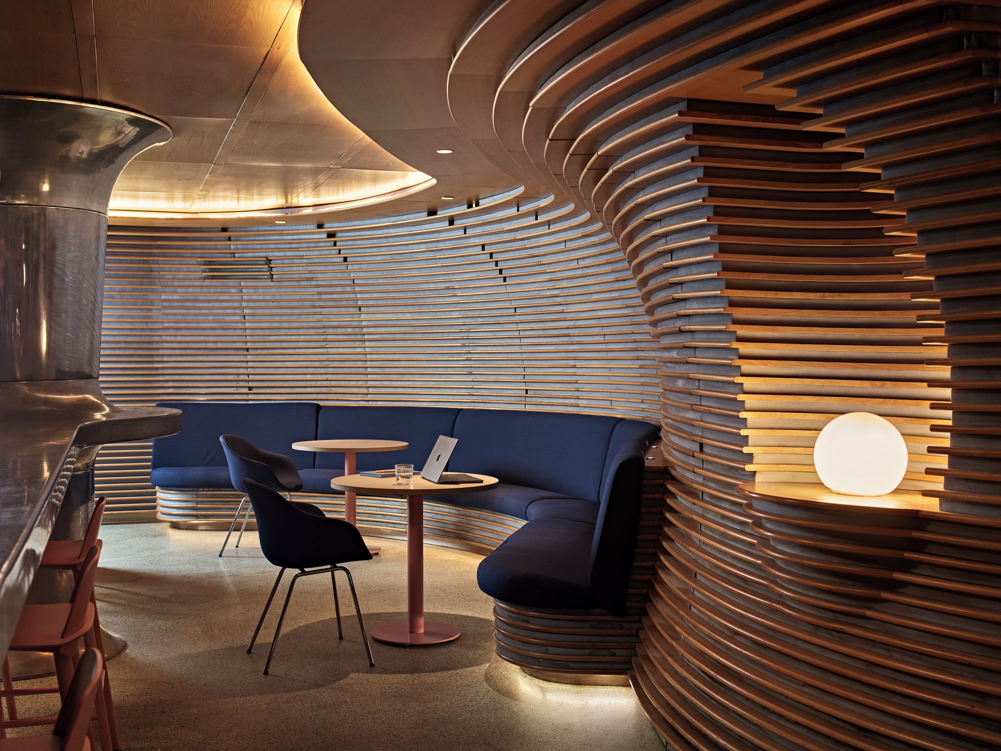 A modern interior with a curved wooden wall, a blue sofa, a round table, and a chair.