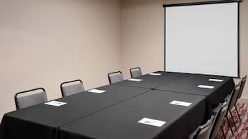 Ein Konferenzraum mit einem langen Tisch, sechs Stühlen und einer Projektionsleinwand.