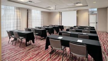 A conference room with multiple tables and chairs, a projector screen, and a large window with curtains.
