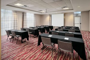 A conference room with multiple tables and chairs, a projector screen, and a large window with curtains.