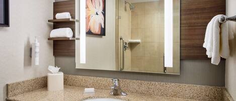 Baño con encimera de granito, lavabo blanco, espejo grande, cuadro floral enmarco y toallero con toalla blanca.
