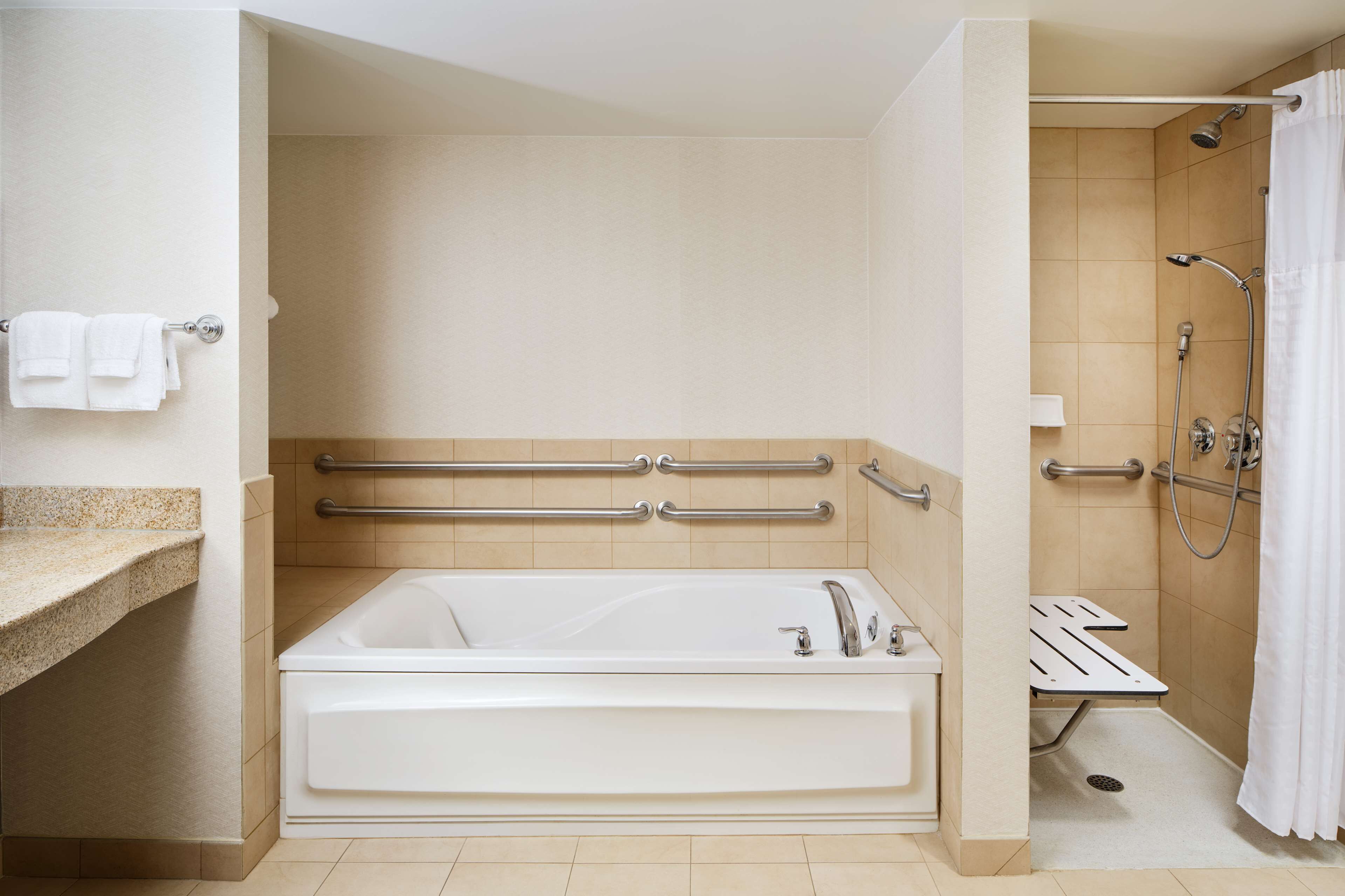 A modern bathroom with a bathtub, shower, and handrails.