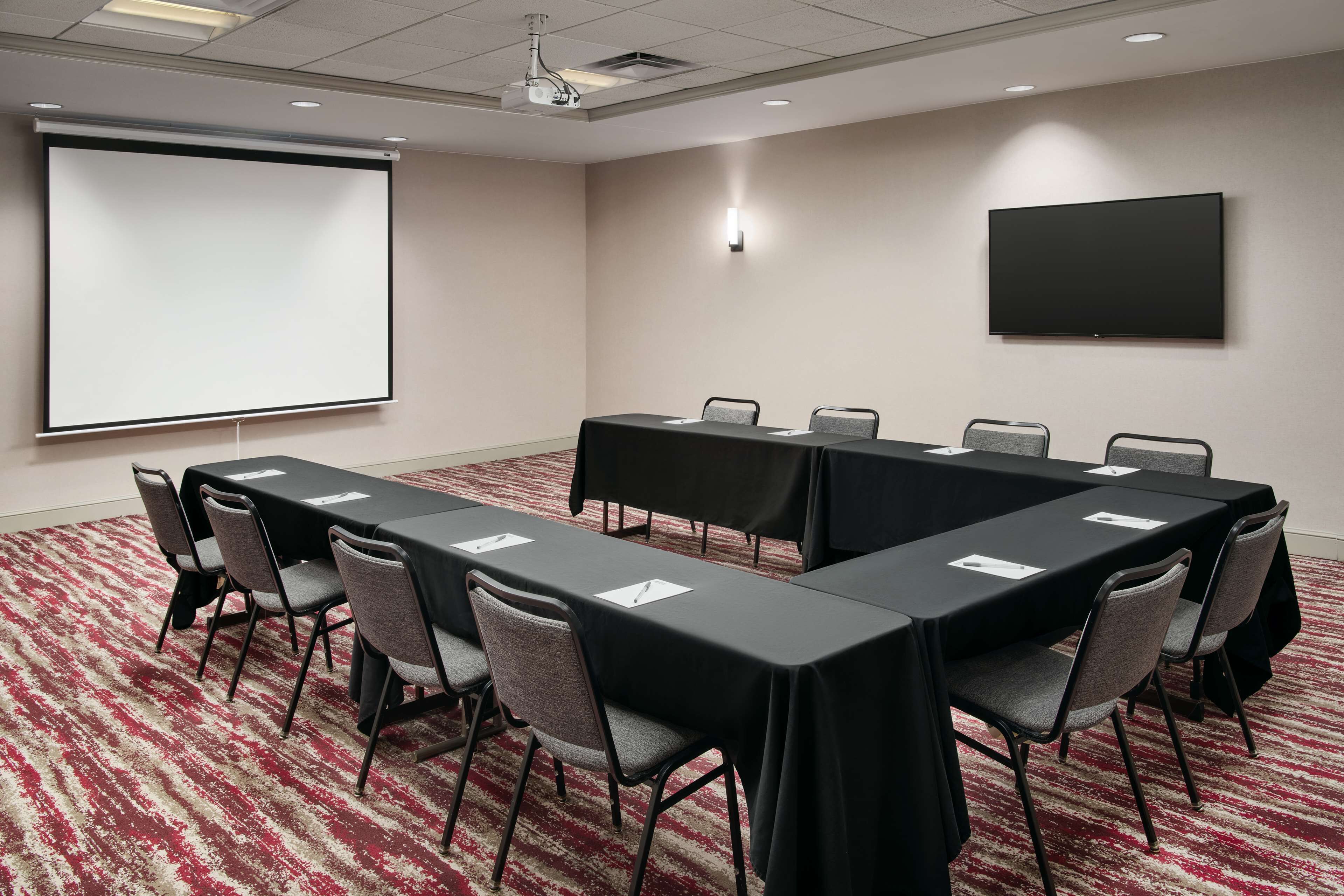 A conference room with a long table, chairs, a projector screen, and a TV.