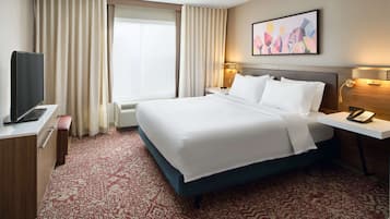 A hotel room with a large bed, a TV, a desk, and a window with curtains.