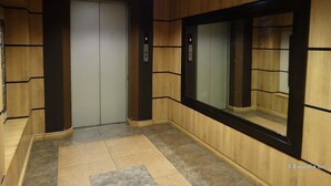 Un ascenseur doté d’un écran numérique affichant le chiffre 3, encadré de panneaux en bois et surmonté d’un sol carrelé.
