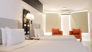 Une chambre d’hôtel avec un grand lit, deux fauteuils, une table de chevet avec une lampe et une armoire.