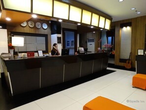 A reception desk with clocks, a telephone, and a laptop. There is a potted plant and a guitar in the background. - Majestic Hotel (formerly Octagon Mansion Hotel) (Manila)