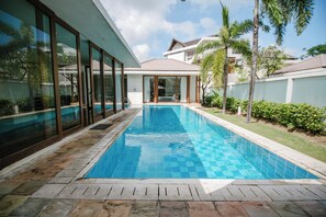Une piscine moderne à l’eau d’un bleu cristallin, entourée d’une terrasse en pierre et de panneaux de verre.