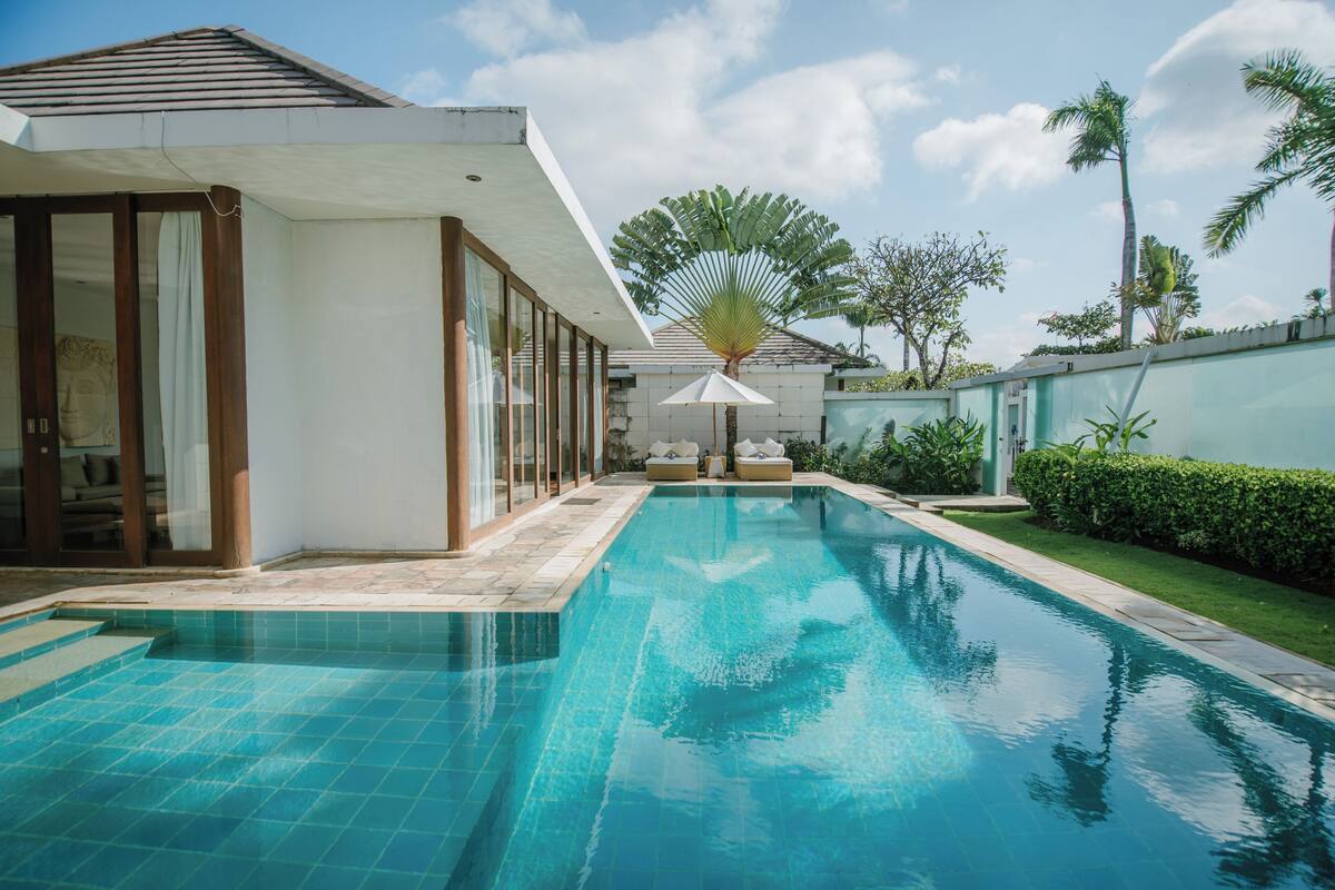 Área de piscina com uma casa moderna, janelas amplas e uma palmeira.